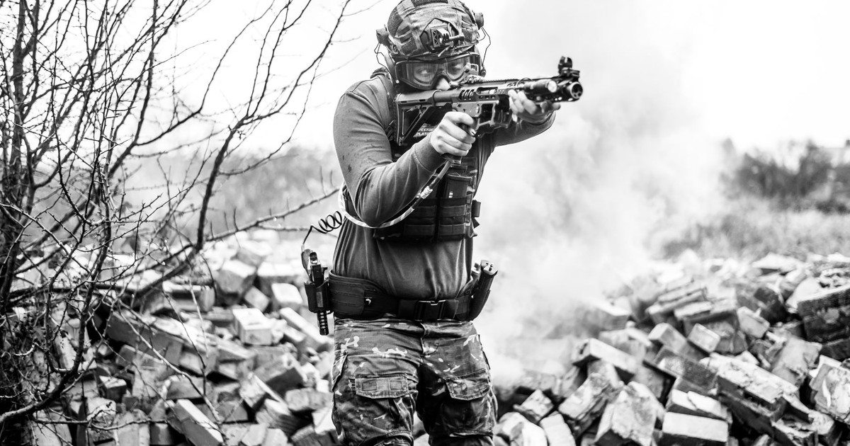 A soldier in full gear aims his rifle during a tactical training session on a rubble-strewn field.
