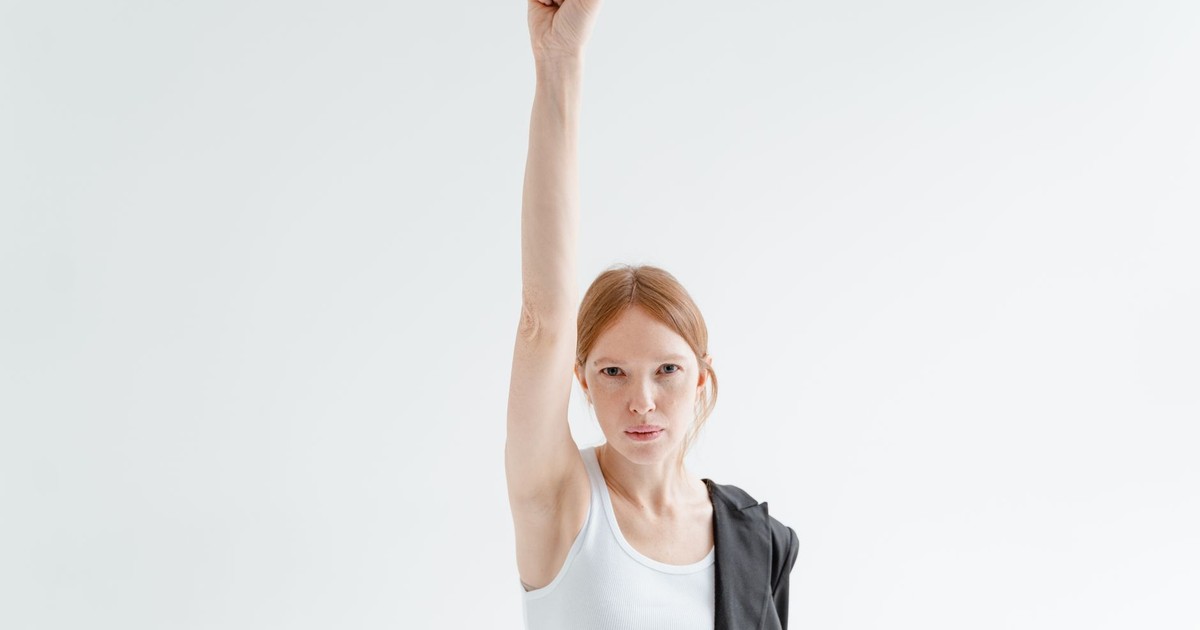 A woman in a white tank top raises her fist in a powerful gesture of strength and equality.