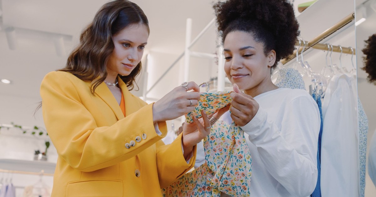 Two women shopping fashionably at a boutique, choosing colorful dresses indoors.