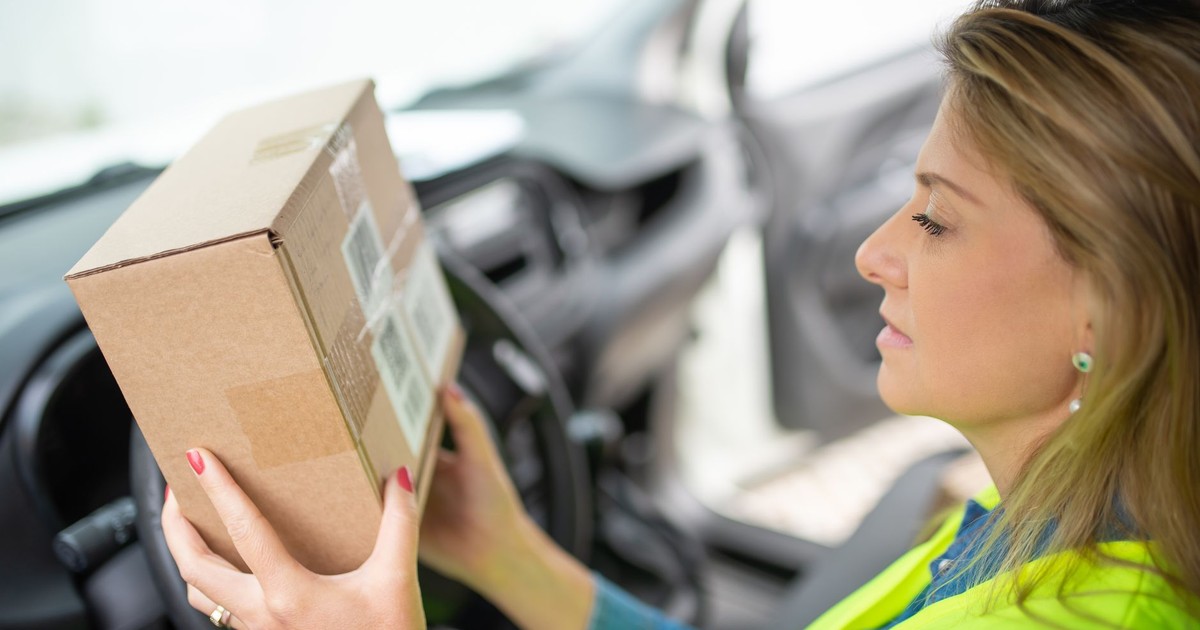 A woman courier checks a delivery package while seated inside a car, ready for distribution.