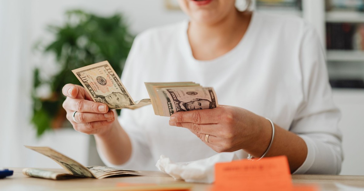 A woman sits indoors counting cash at her office desk, focusing on finances.