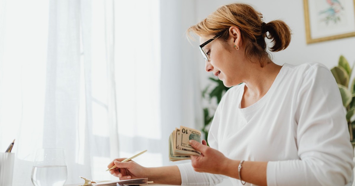 Businesswoman calculating finances with cash, calculator, and notebook at a bright desk.