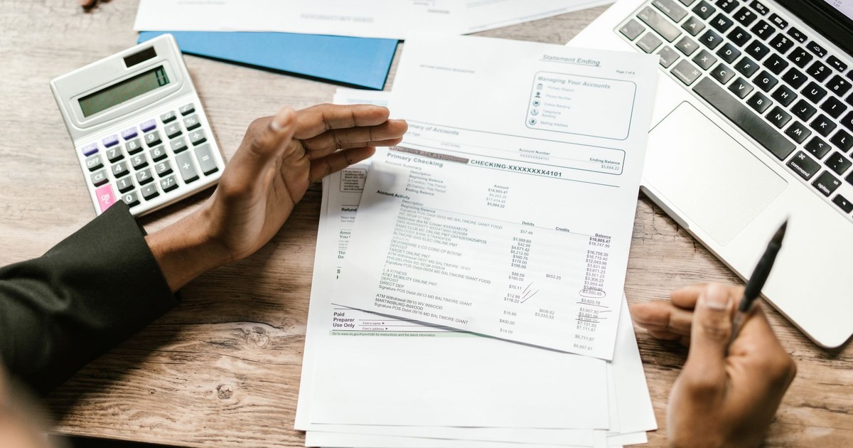 Hands holding financial documents with calculator and laptop on office desk, business analysis scene.
