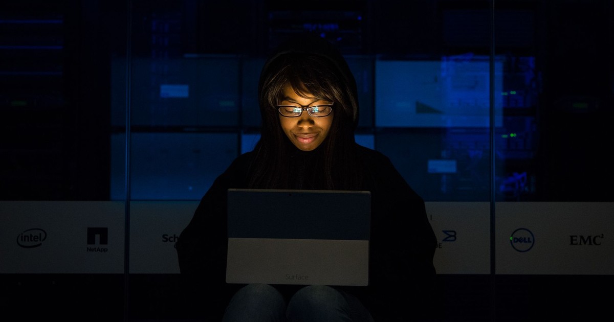 A woman uses her laptop in a dimly lit server room, focusing on technology and work.