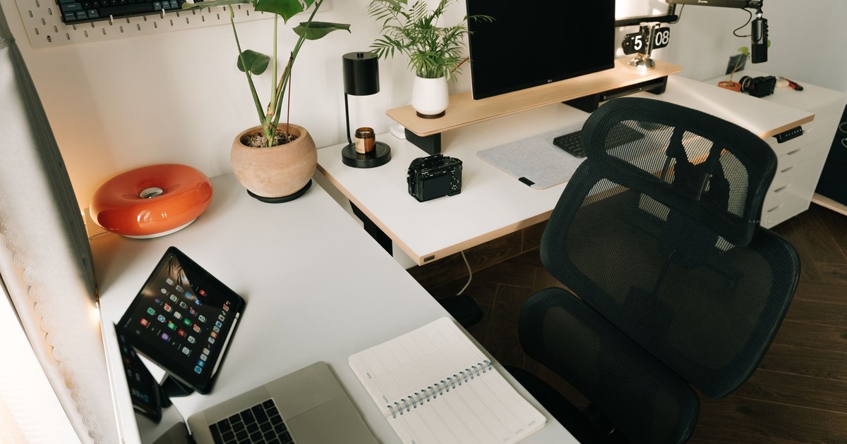 A stylish home office setup featuring tech gadgets, a monitor, a tablet, and decorative plants in a minimalist design.