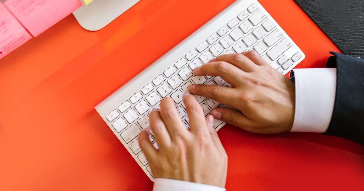 Close-up of hands typing on a wireless keyboard on an orange desk, ideal for tech and business themes.
