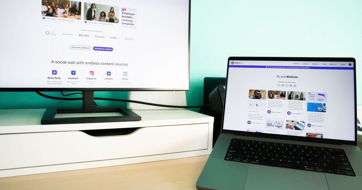 Office desk workspace with a laptop and a monitor displaying a social media wall solution.