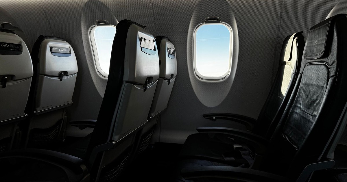 Interior of an empty airplane cabin with a bright sky visible through the window.
