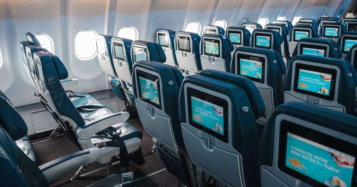 Empty airplane interior highlighting rows of seats with touchscreens, offering a modern in-flight experience.