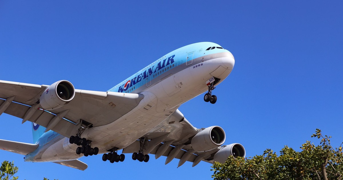 A large airliner flying low against a clear blue sky, captured in daytime.
