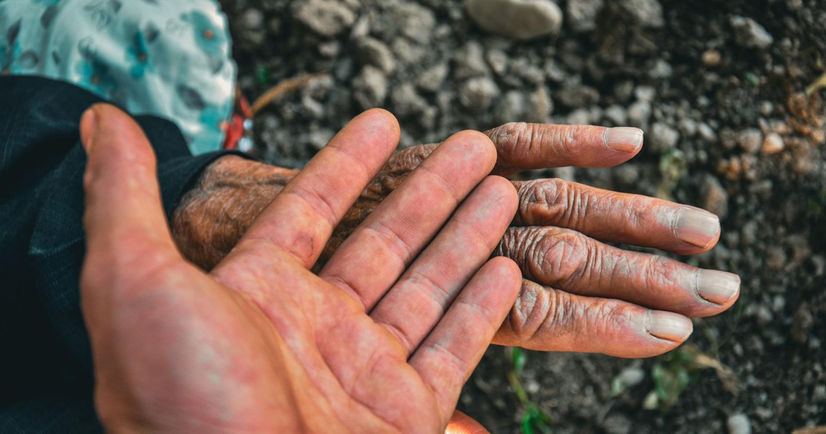 Close-up of young and old hands symbolizing generational connection and unity outdoors.