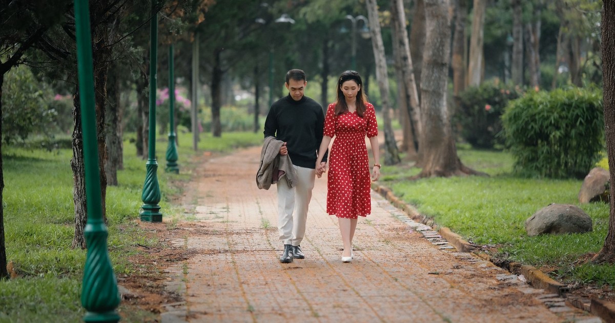 A couple walks hand in hand along a scenic park pathway surrounded by greenery.