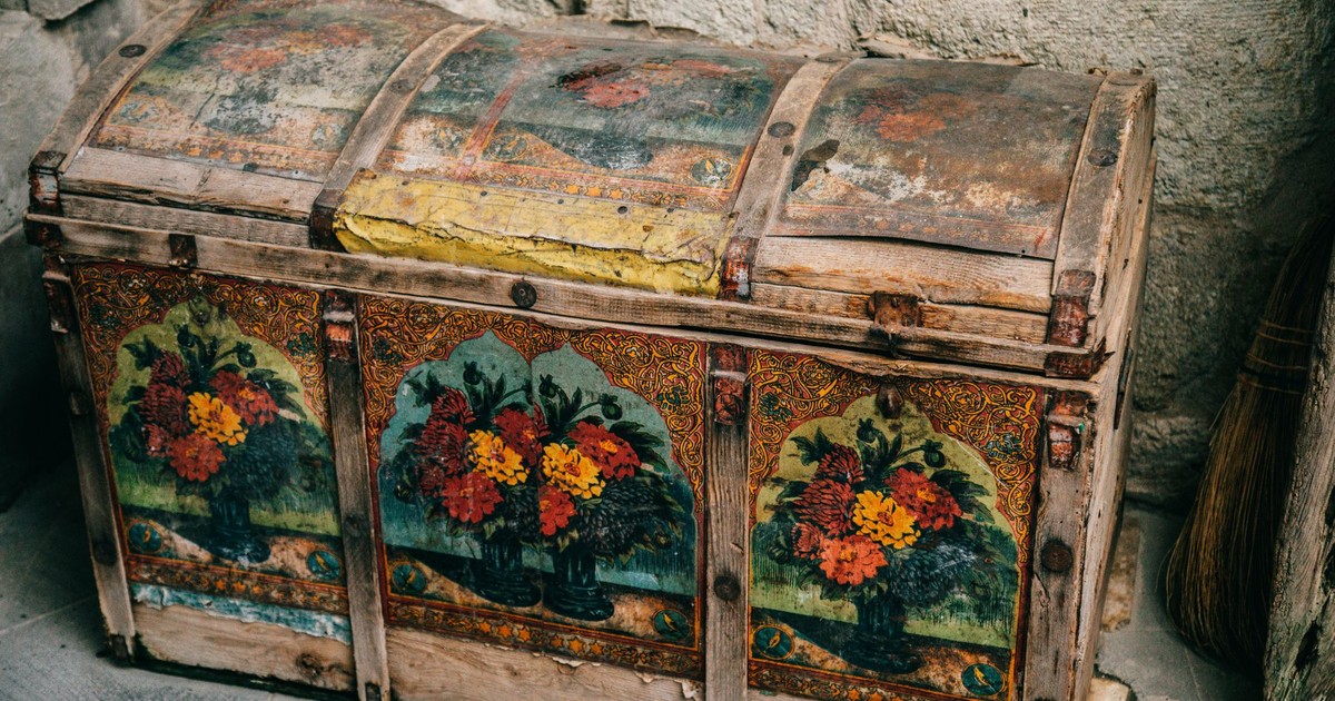From above of aged shabby wooden box with colorful ornaments and elements placed near stone wall on ground in ancient city