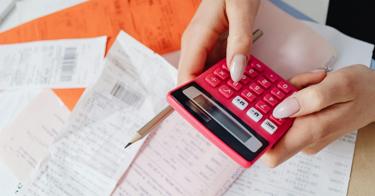 Hands using a pink calculator to manage expenses amidst various receipts and documents.