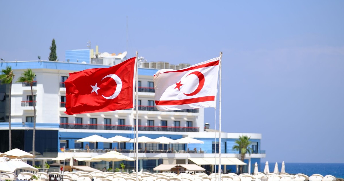 Turkish and Northern Cyprus flags waving at a coastal resort with a beach setting.