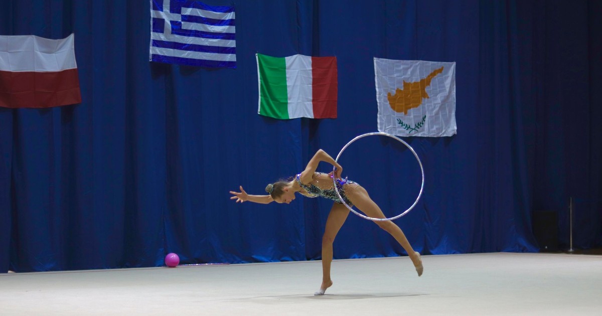 Dynamic image of a gymnast performing with a hoop on an international stage.