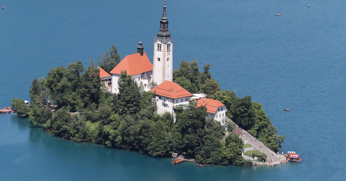 Stunning aerial view of Bled Island and church on Lake Bled, Slovenia, surrounded by crystal blue water and lush greenery.