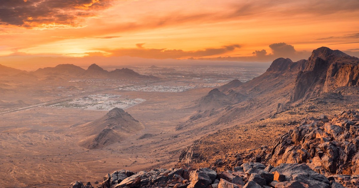 Panoramic view of rocky desert landscape in Medina, Saudi Arabia at sunset, showcasing vibrant sky and mountains.