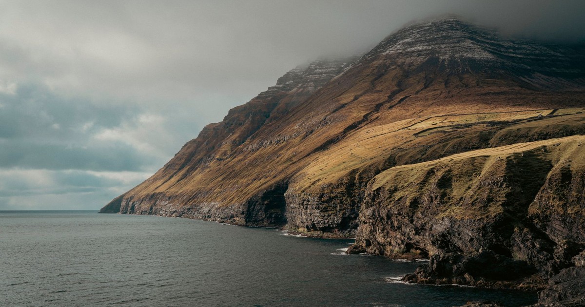 Misty cliffs of Faroe Islands with dramatic coastal scenery under a cloudy sky.