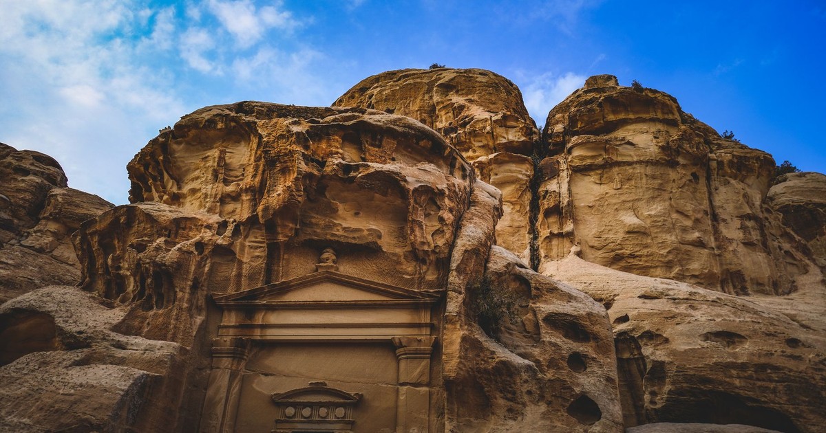 Explore the antiquity of Petra with this stunning image of a rock-carved triclinium against a vibrant blue sky.