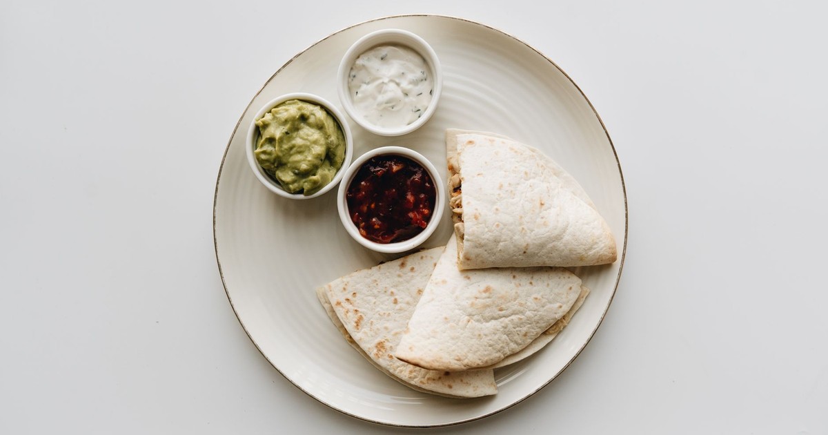 A top view of a Mexican quesadilla served with guacamole, salsa, and sour cream on a plate.