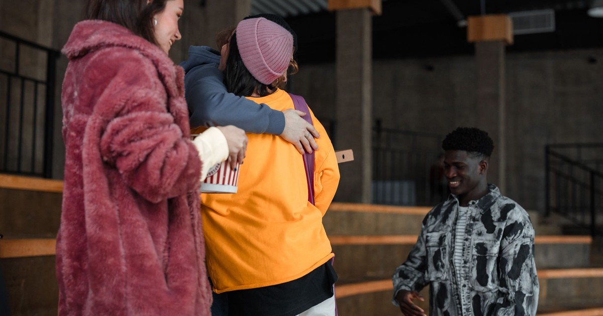 A group of friends hugging and smiling indoors, showcasing diversity and happiness.