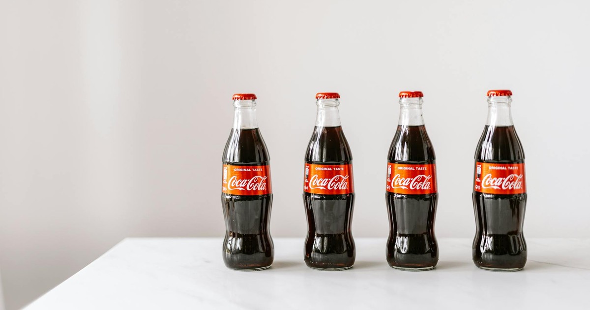 Glass bottles full of fresh soft drink placed on white table in row