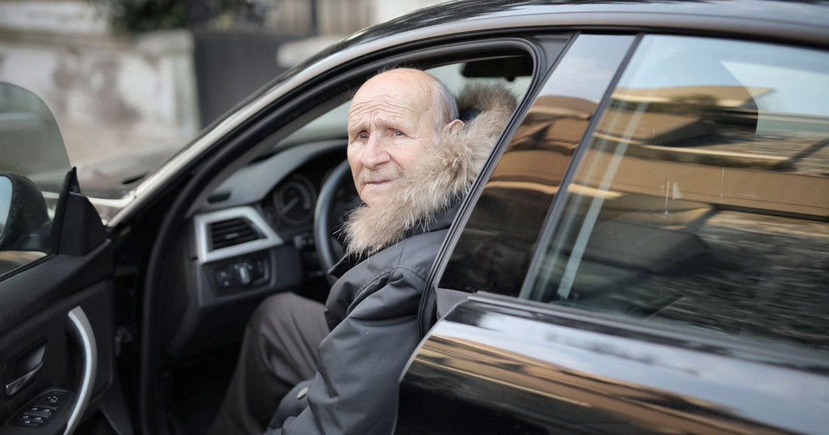 An elderly man in a winter coat stepping out of a parked car outdoors.