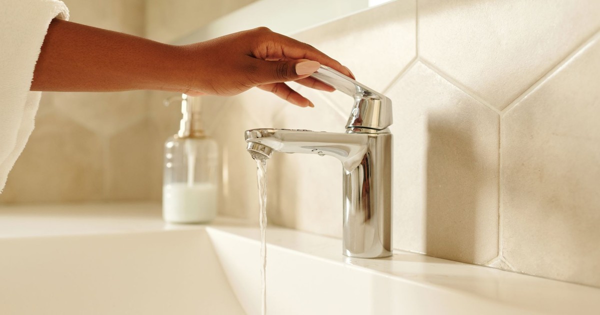 A close-up shot of a hand operating a chrome bathroom faucet with water flowing in a modern bathroom setting.