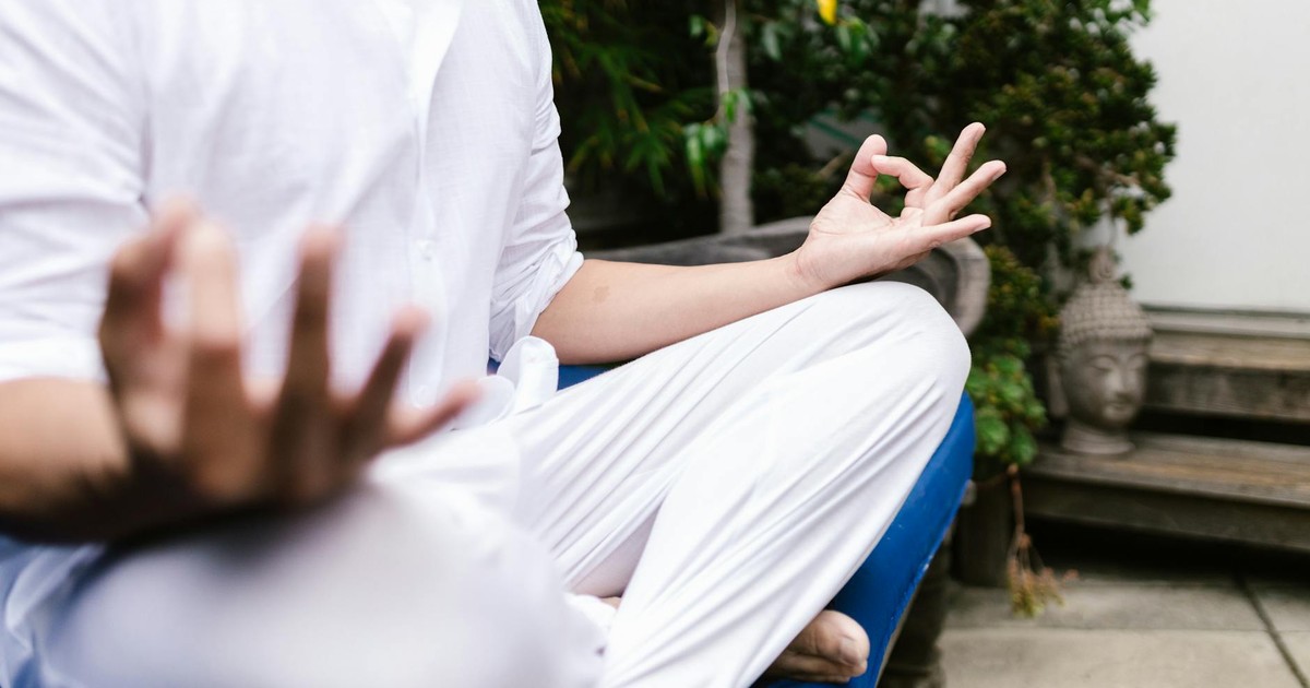A person in white practicing yoga meditation outdoors in a serene environment.