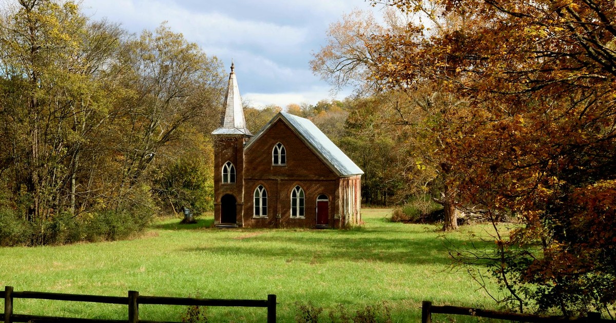 A quaint church in a serene autumn setting surrounded by colorful foliage and green fields.