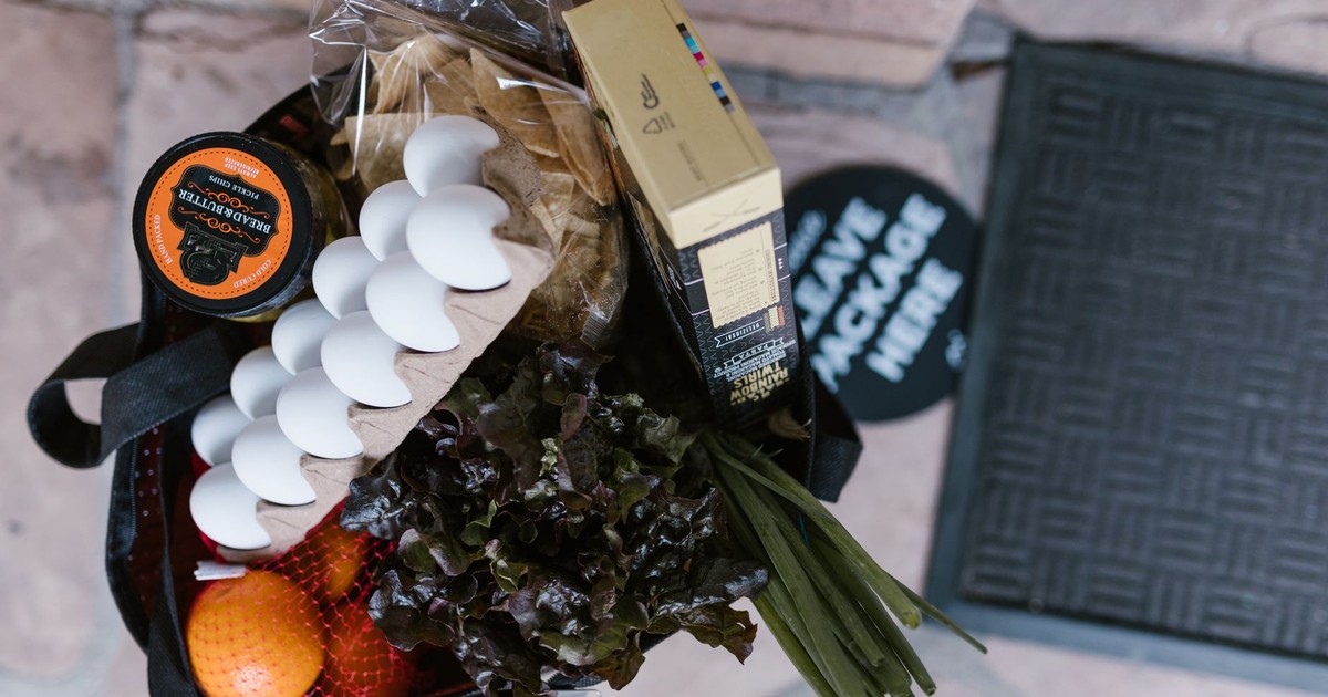 Overhead shot of fresh groceries including eggs, vegetables, and oranges in a reusable bag.