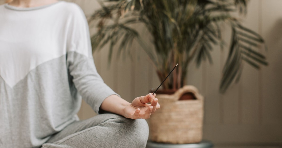 Woman meditating indoors holding incense, promoting relaxation and calm.