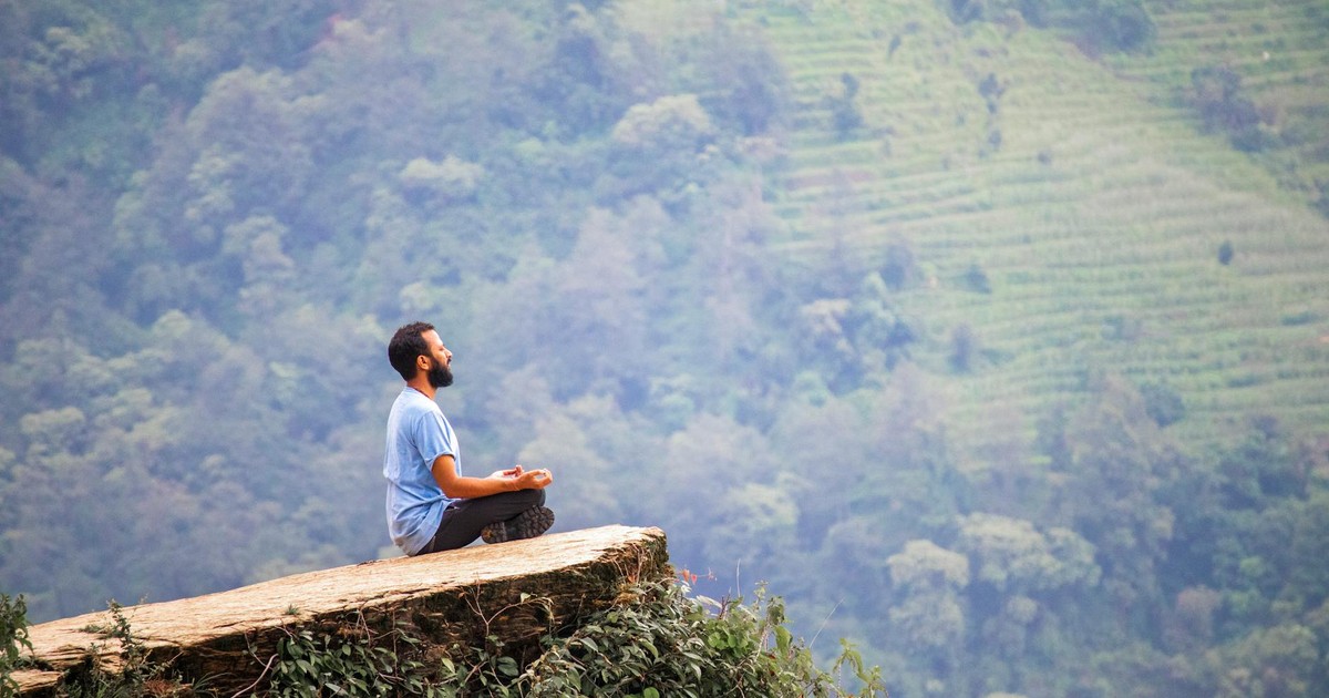 Man meditating on a cliff with lush green mountains in Ghandruk, Nepal.
