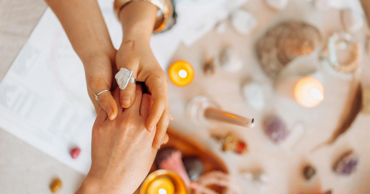 Hands exchanging energy with crystals and candles on a mystic table setting.