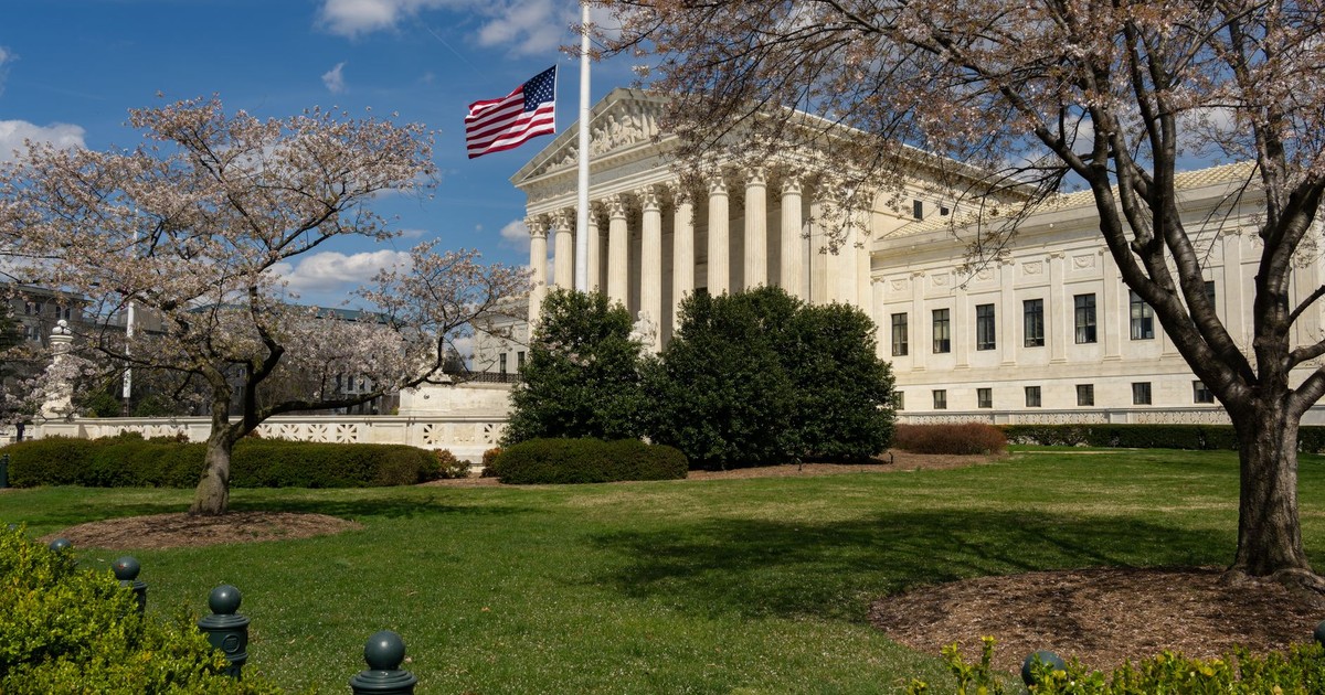 A view of a neoclassical government building with an American flag and cherry blossoms in Washington, DC.