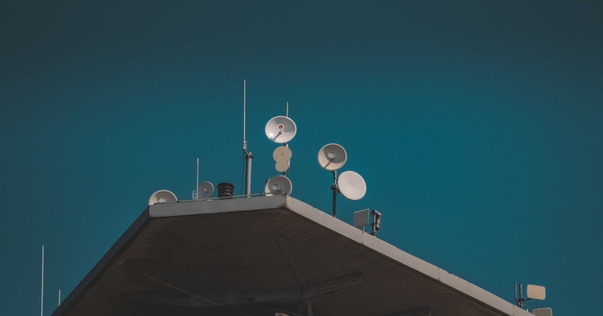 A low-angle view of communication dishes and antennas on a building against a clear blue sky.