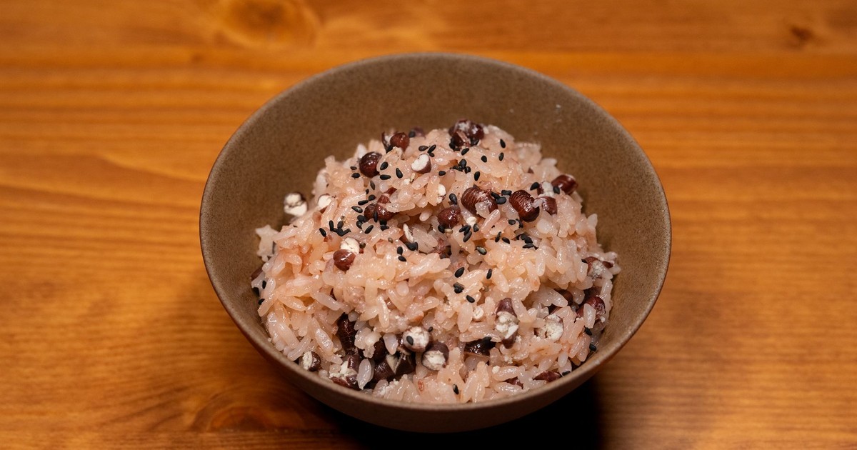 Appetizing bowl of traditional sticky rice mixed with beans and sesame seeds on a wooden surface.