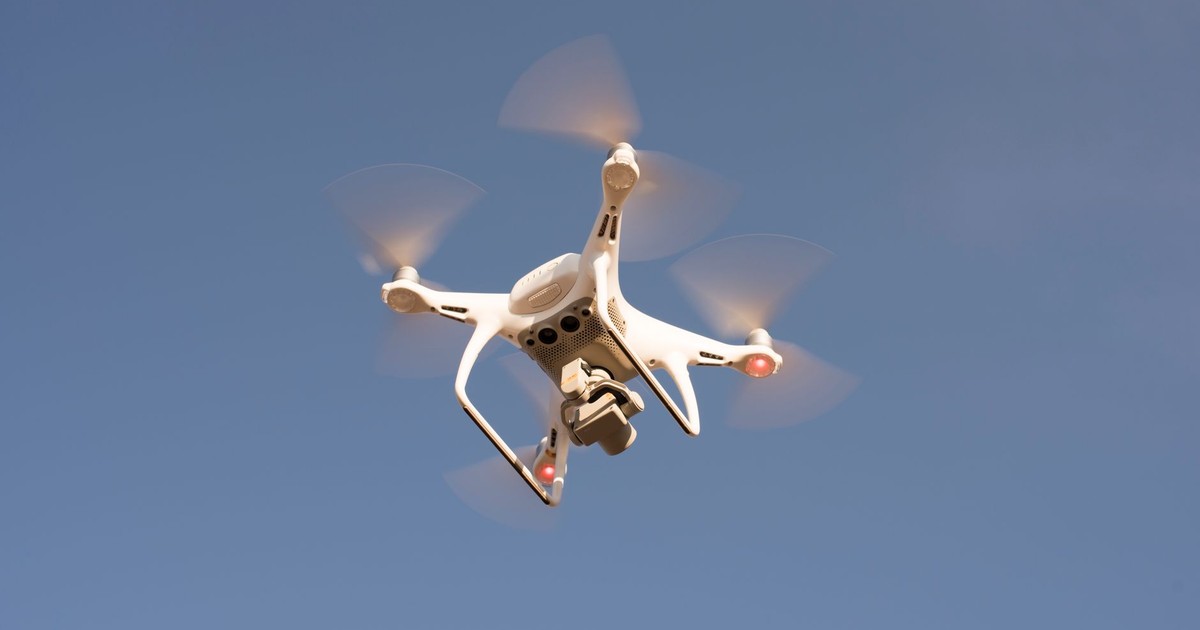 A white drone in flight against a clear blue sky, capturing aerial footage with precision.