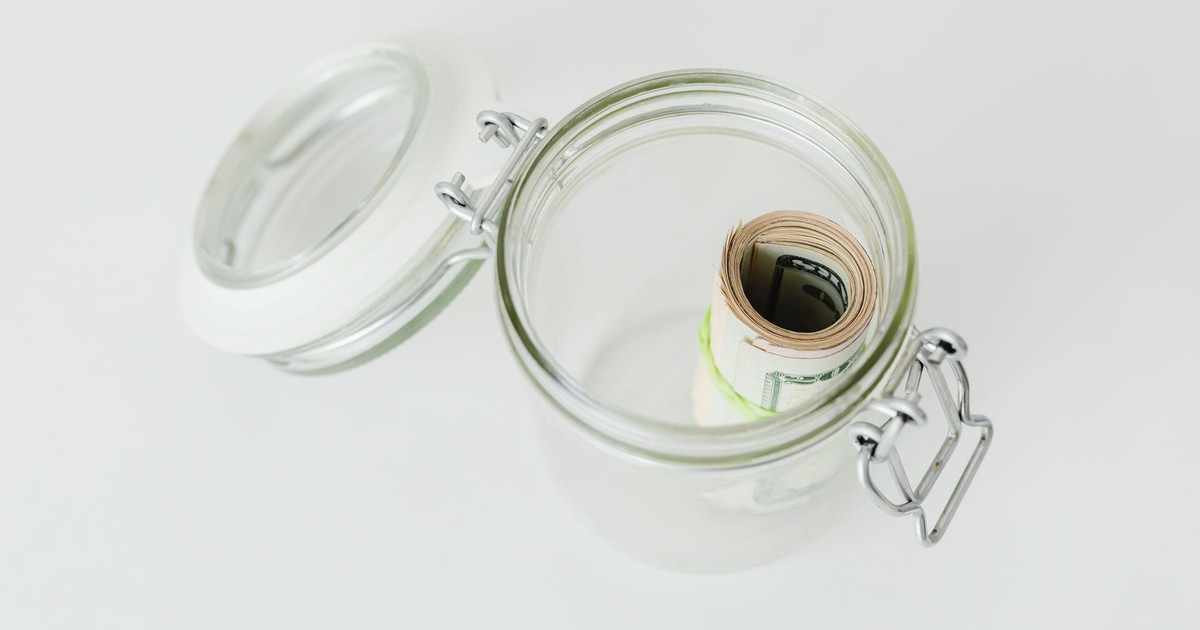 Close-up shot of rolled US dollar bills inside a glass jar on a white surface.