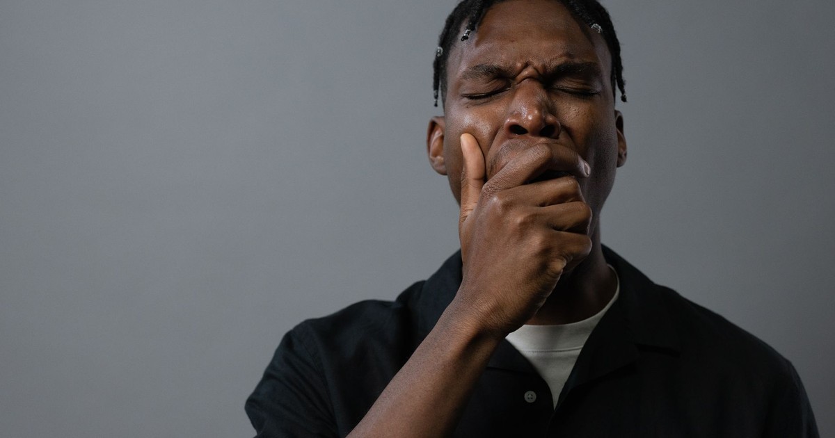 Portrait of a tired man yawning with hand on mouth, showing fatigue and exhaustion.