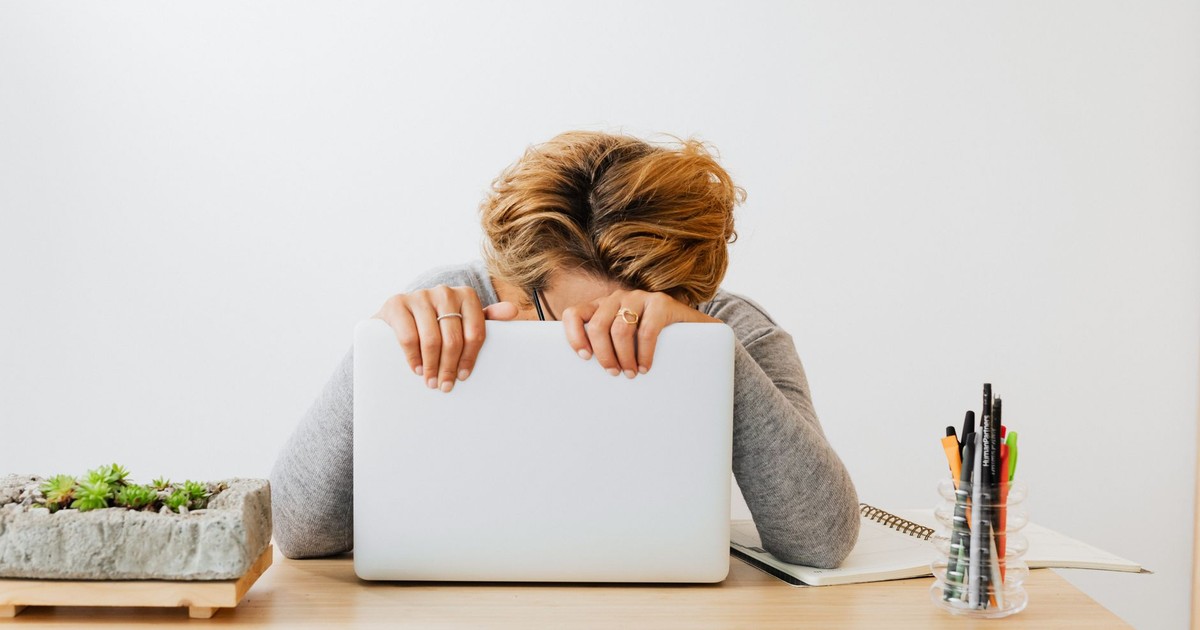 Woman wearing gray sleeves, leaning on laptop with head down in modern workspace.