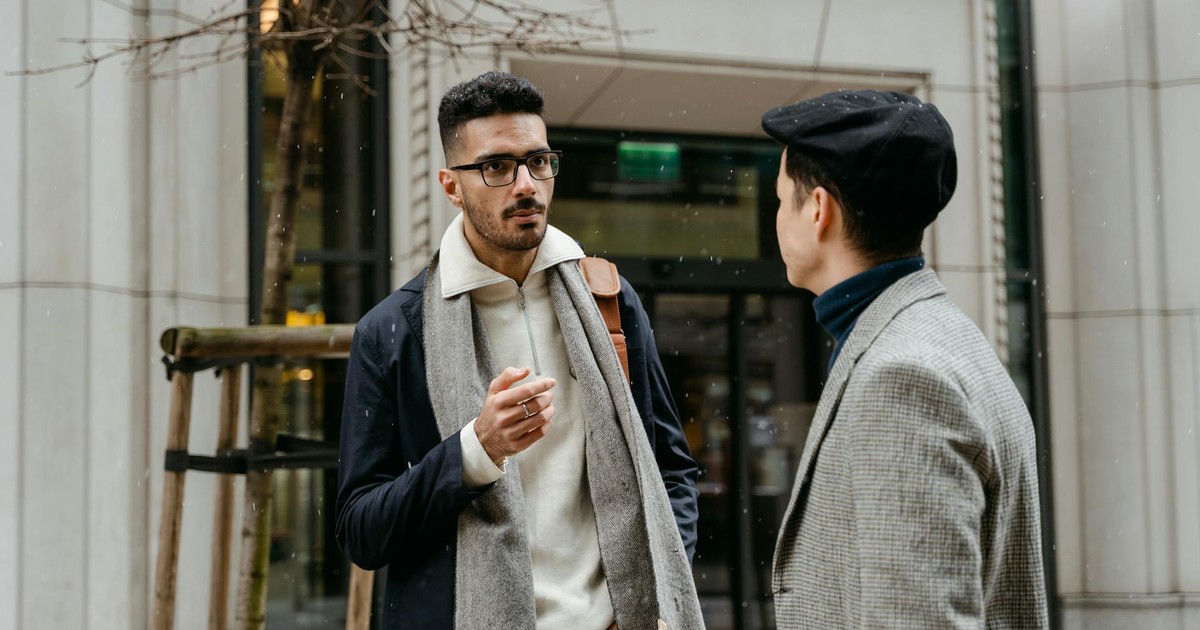 Two businessmen engaged in conversation outside in winter attire with snow falling lightly.