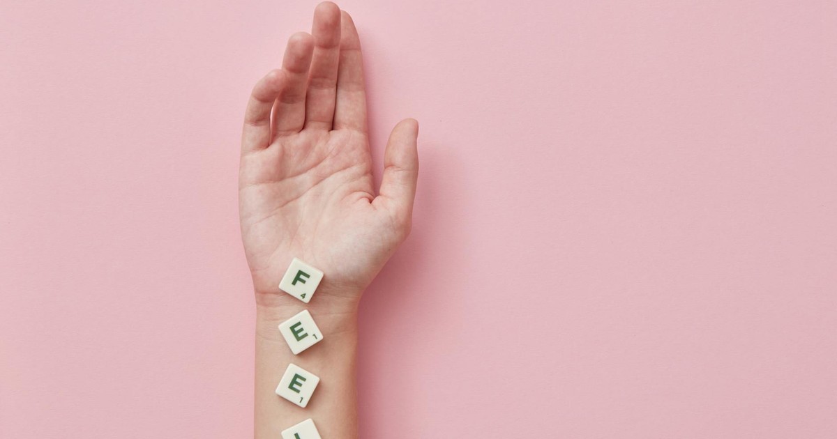 A minimalist photograph of a hand laid on pink background spelling 'FEEL' with Scrabble tiles.