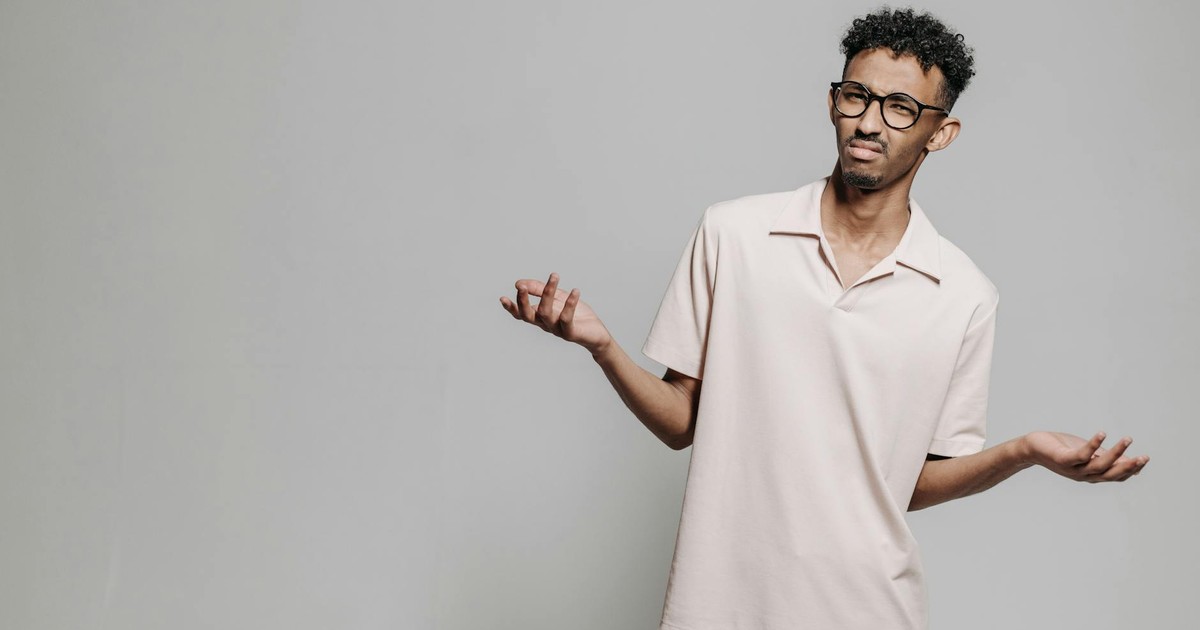 Studio portrait of a young African American man wearing eyeglasses and a white polo shirt expressing confusion.