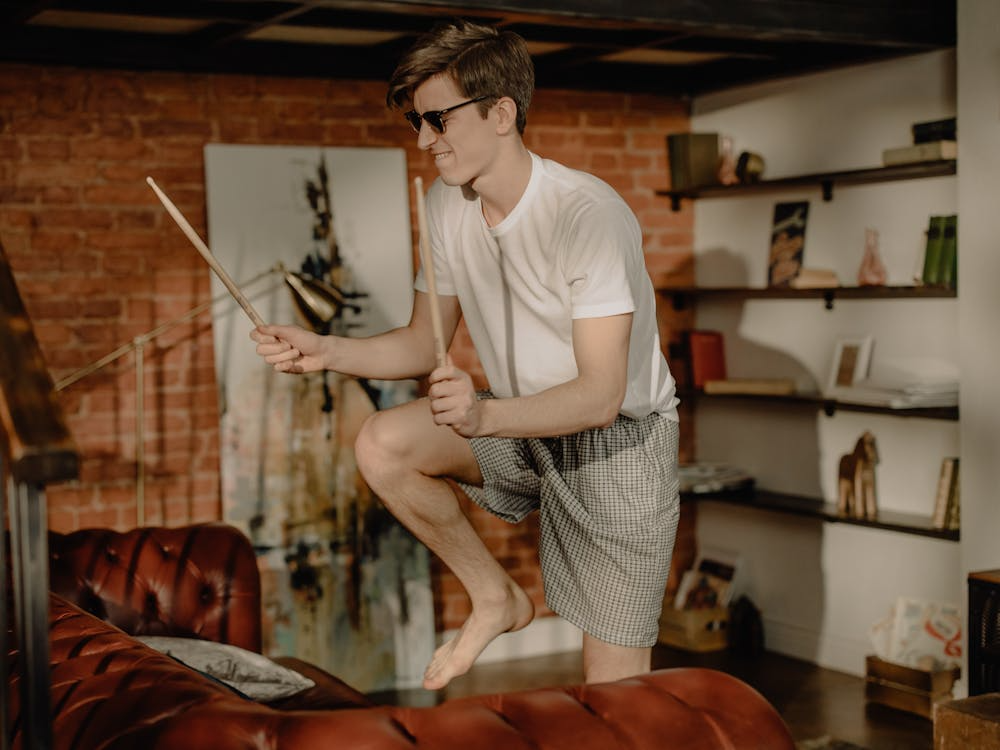 man wearing sunglasses drumming with sticks in a cozy home setting