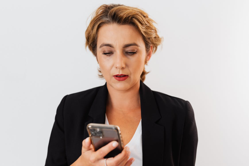 Businesswoman in blazer focused on smartphone, isolated on white background.
