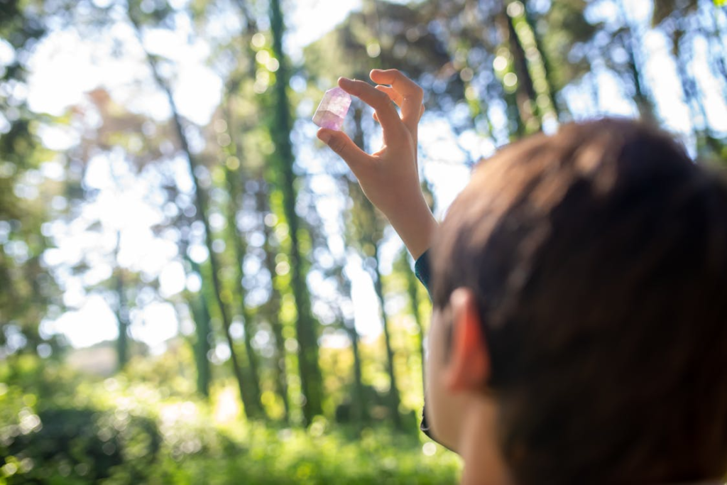 A young individual closely examines a gem under the dappled sunlight in a lush forest setting