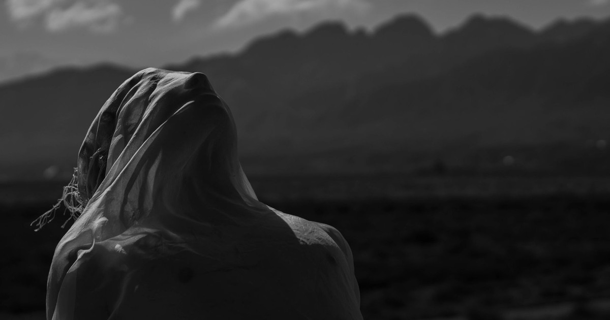 Silhouette of a person draped in cloth with a mountainous background, offering a moody vibe.