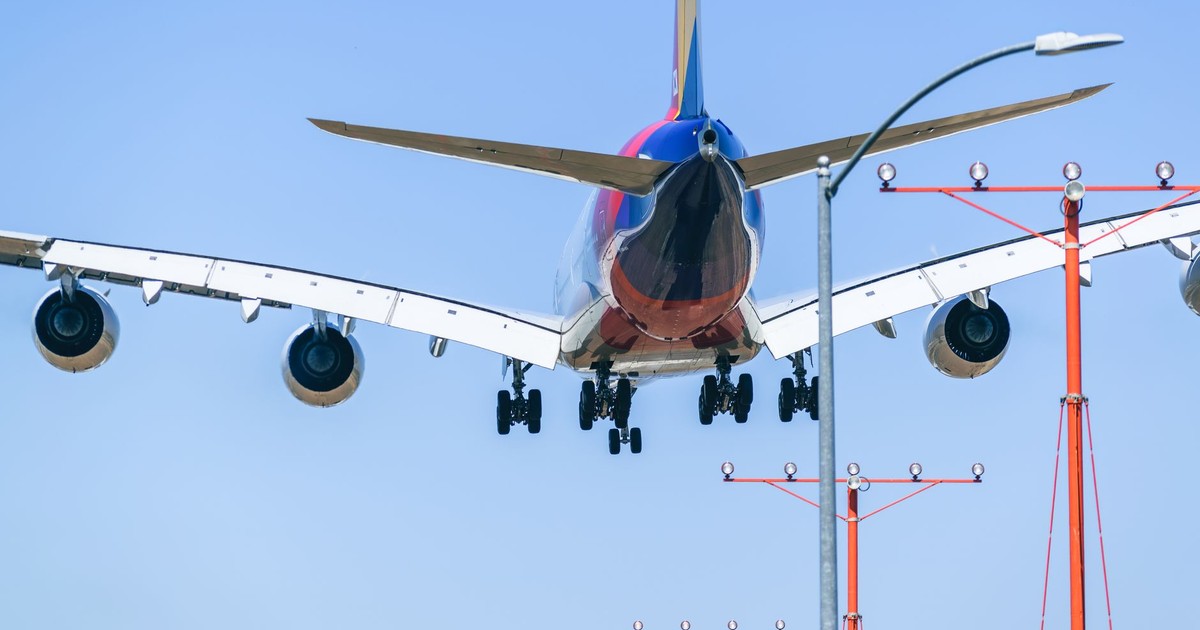 Passenger airplane approaching runway during daytime landing with clear blue sky backdrop.